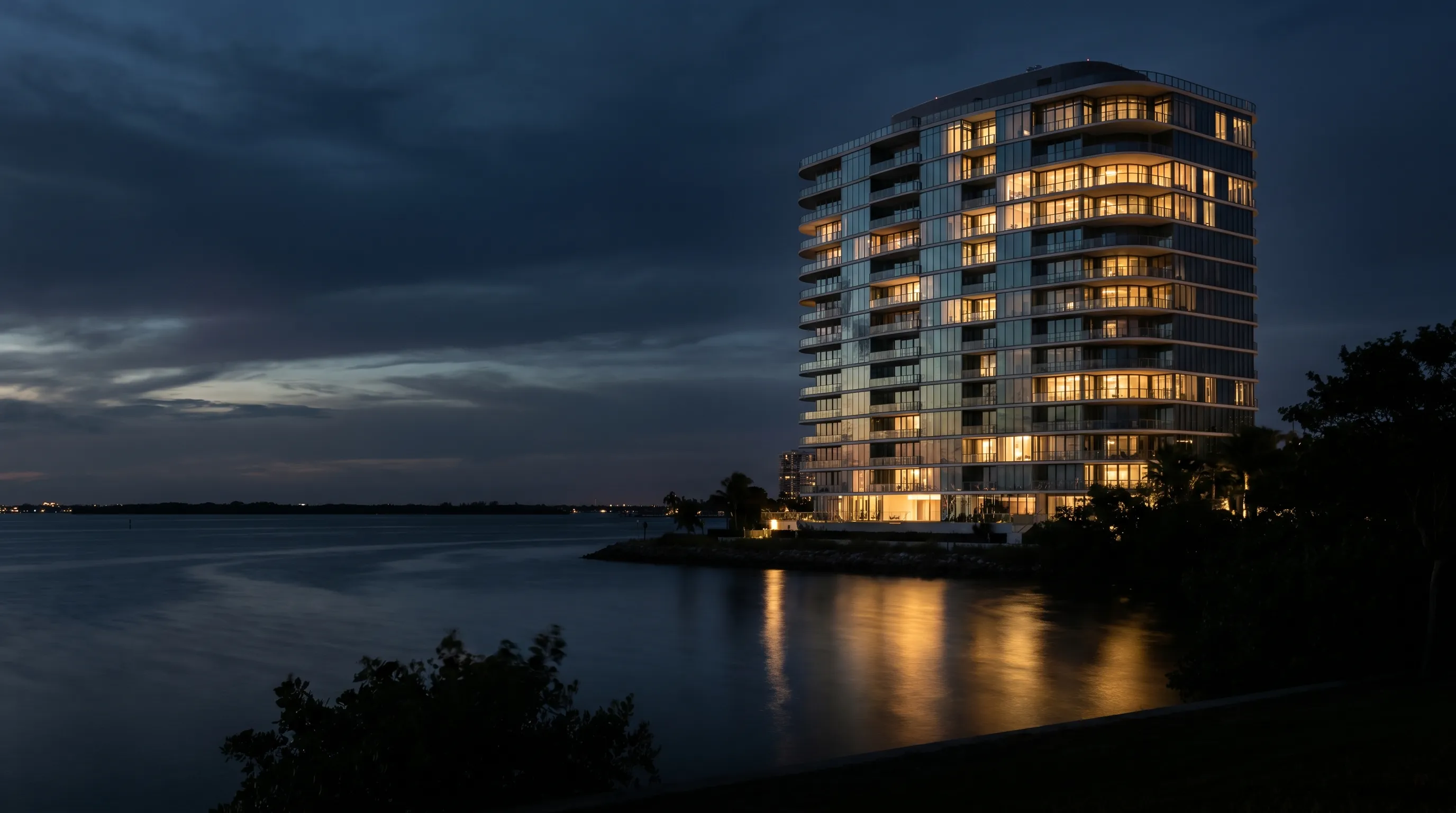 Gold Coast luxury residential tower at dusk, champagne gold light reflecting on dark harbour water below a deep twilight sky